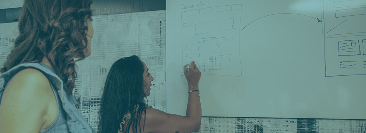 Two people looking at a whiteboard while one of them writes something on it.