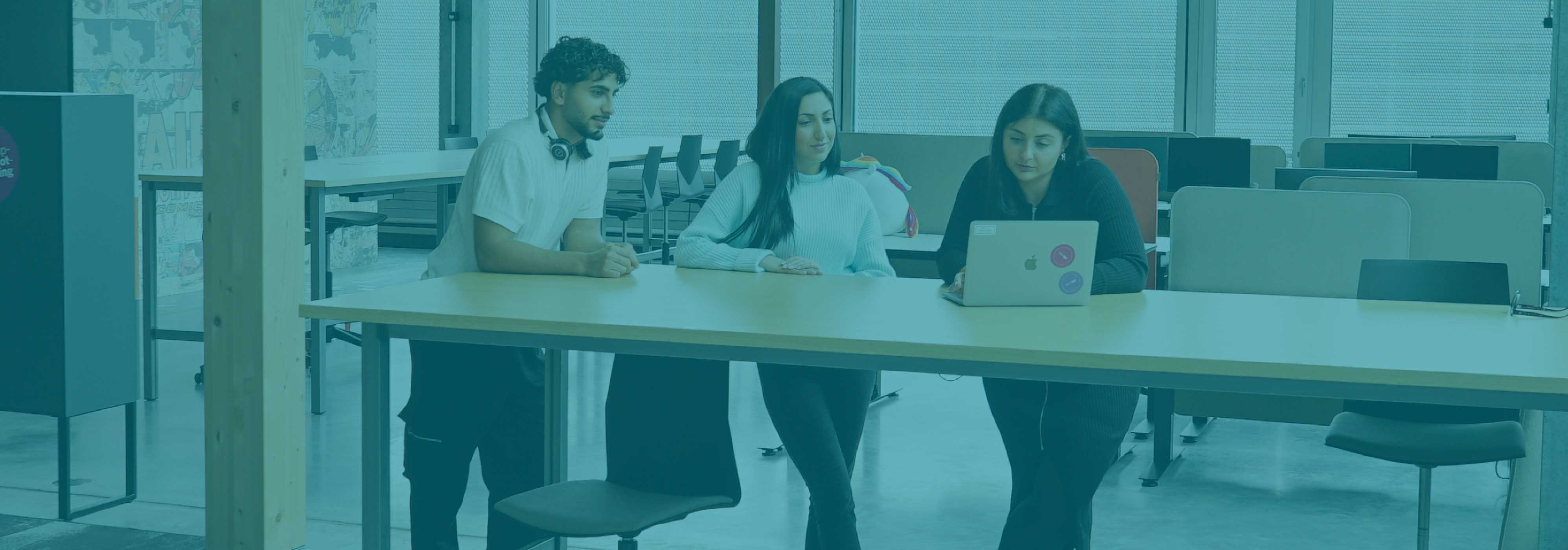 Apprentices discussing something at a desk and looking into a notebook